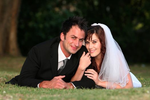 Beautiful wedding couple laying down outdoors on the grass