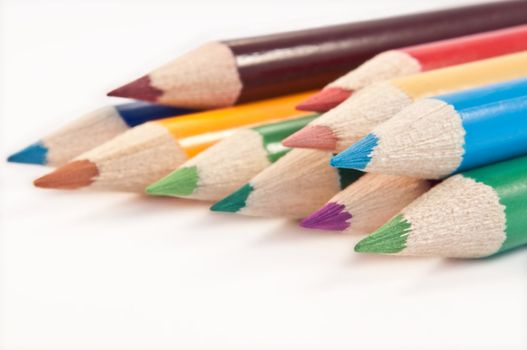Close up capturing a selection of coloured drawing pencils arranged over white.