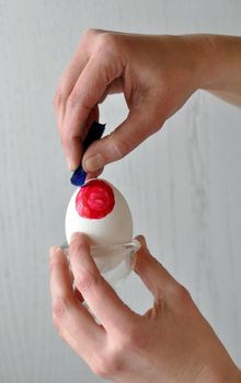 Female hands coloring an easter egg - painting a ladybug on it - behind gray