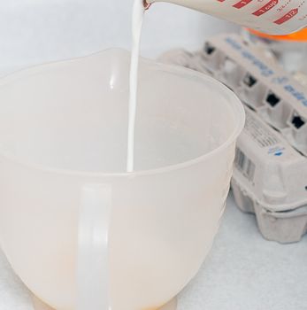 Milk is being measured in a plastic measuring cup