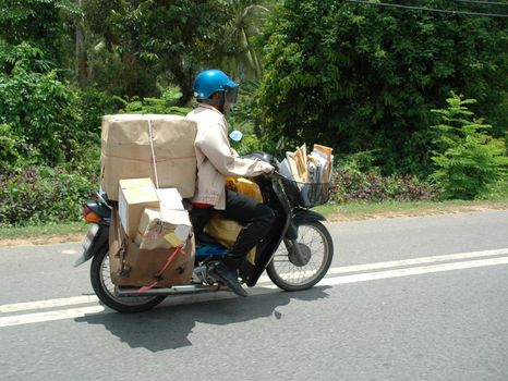 Postman is driving his motorbike. The postman is from Thailand.