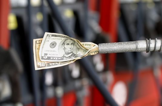 Dollars displayed in a gas pump with pumps in background.