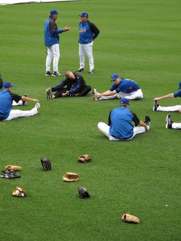Baseball players and pitchers stretch before a game at Citi Field, with gloves scattered