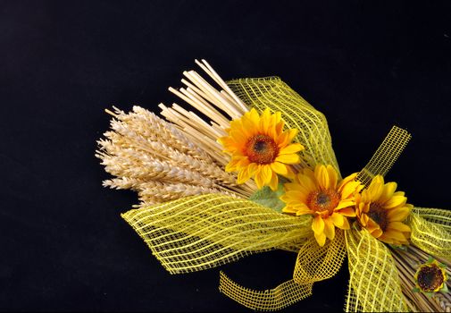 Decoration consists of stalks of wheat and sunflowers on a black background.