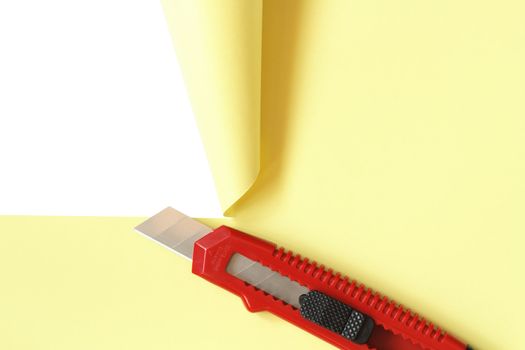 Red office knife cutting yellow paper sheet. Isolated on white with clipping path