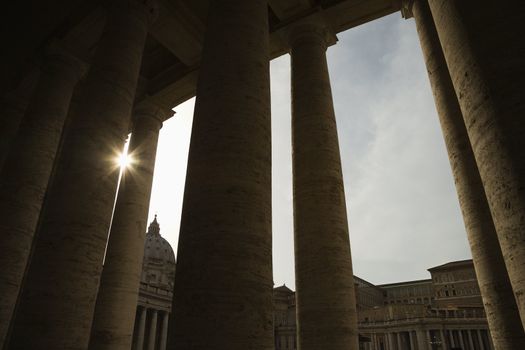 Sun peeking through doric columns in Saint Peter's Square in Vatican City, Italy.