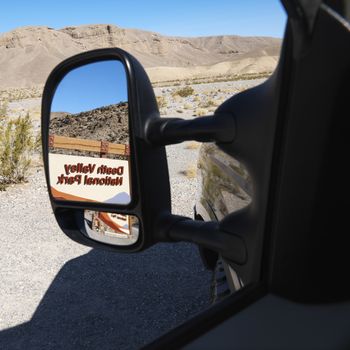 Death Valley National Park entrance sign reflected in side view vehicle mirror.