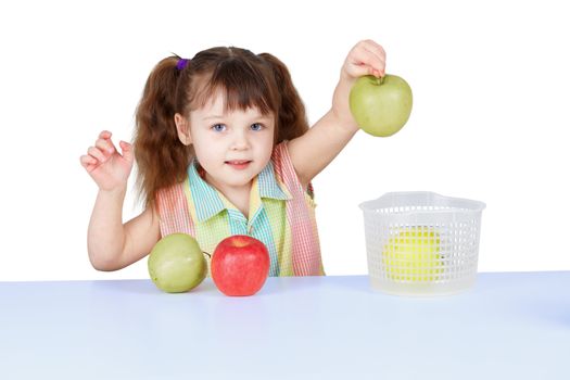 A little girl playing with green apples sitting at the table