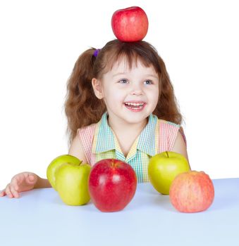 A happy girl playing with apples sitting at the table