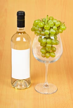 A bottle of wine, a large glass and grapes on wooden background