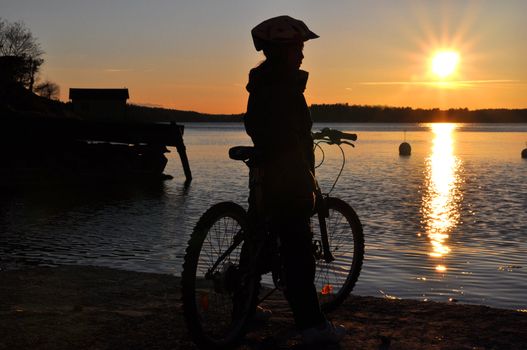 A young girl on a bicyle looking out over a bay during sunset