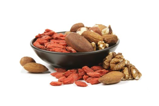 Red dry goji berries with mixed nuts in a small black bowl on a reflective white background
