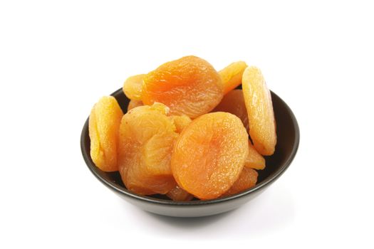 Dried juicy orange apricots in a small black bowl on a reflective white background