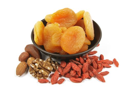 Dried juicy orange apricots with mixed nuts and goji berries in a small black bowl on a reflective white background