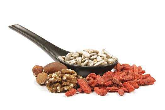 Sunflower seeds on a black spoon with mixed nuts and goji berries on a reflective white background