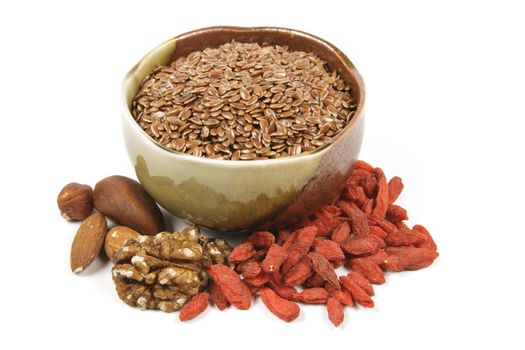 Bown linseed seeds in a small brown and green bowl with mixed nuts and goji berries on a reflective white background