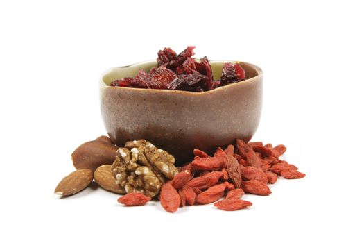 Red ripe dried cranberries in a small green and brown bowl with mixed nuts and goji berries on a reflective white background