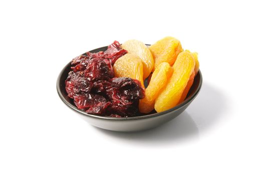 Red ripe dried cranberries and dried apricots in a small black bowl on a reflective white background