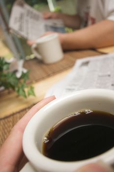 Morning Coffee Macro of Cup with man reading newspaper in background.