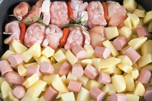 detail of raw pork kebab with sliced potatoes, wurstel and rosemary