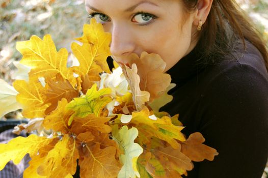 beautiful woman's eyes looking through autumn leaves