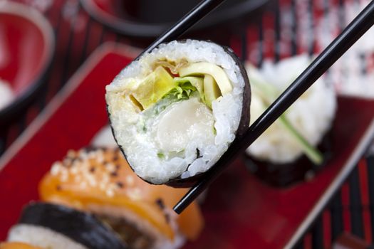 Tuna roll on square green plate with wasabi and ginger. Soy dipping bowl in background. Shot with very shallow depth of field