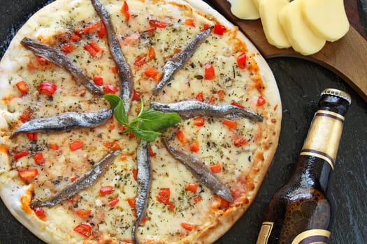 Anchovies pizza with a bottle of beer and ingredients