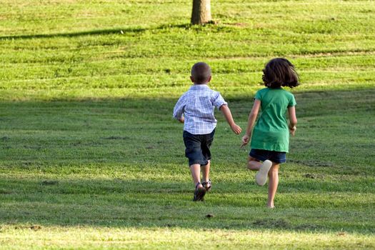 A little boy and girl run through the grassy field without a care in the world.