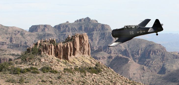 An old military prop plane flies low over a desert landscape in the superstition mountains of Arizona. Taken from on top of the flatiron.