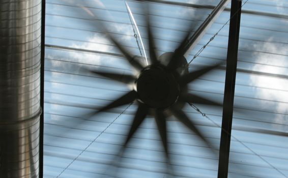 A giant fan in an industrial setting. The open sky can be seen through a sun screen.