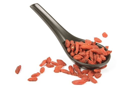 Red dry goji berries on a black spoon with a reflective white background