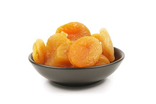 Dried juicy orange apricots in a small black bowl on a reflective white background