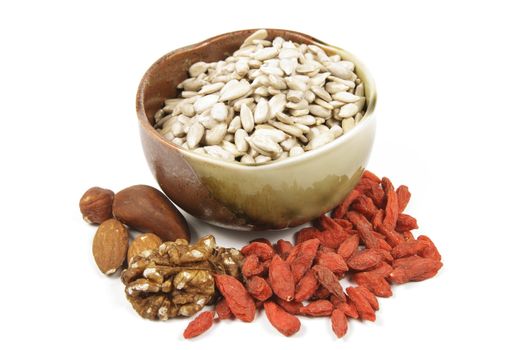 Sunflower seeds in a brown and green bowl with mixed nuts and goji berries on a reflective white background