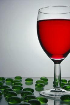 Wine glass filled with red wine, with green glass pebbles scattered around