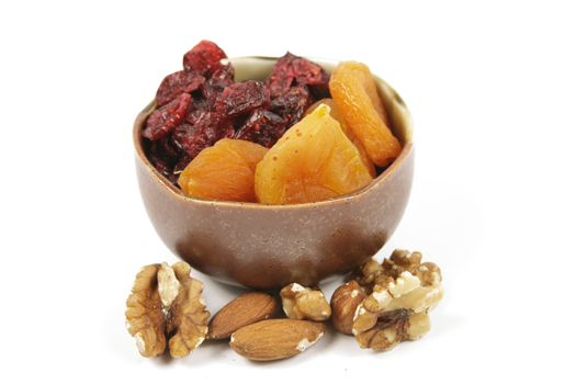 Red ripe dried cranberries and dried orange apricots in a small bowl with mixed nuts on a reflective white background