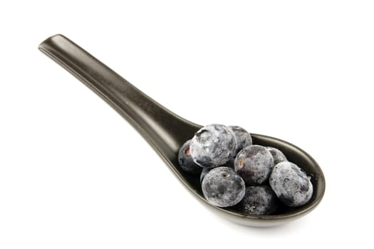 Blue ripe blueberries on s amll black spoon with a reflective white background