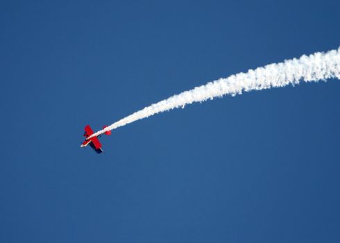 A stunt airplane performs a inverted roll at an airshow. Bright blue sky