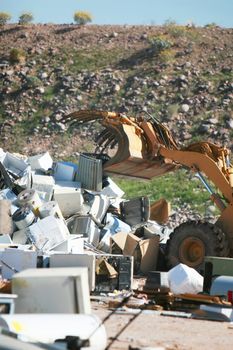 A bulldozer crushes and moves a giant stack of refrigerators, air conditioners, and stoves.