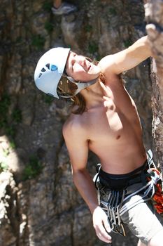 A teenager climbs a steep rock face. He is wearing a harness and helmet. This is sport lead climbing using quickdraws to clip into bolts on the rock. 