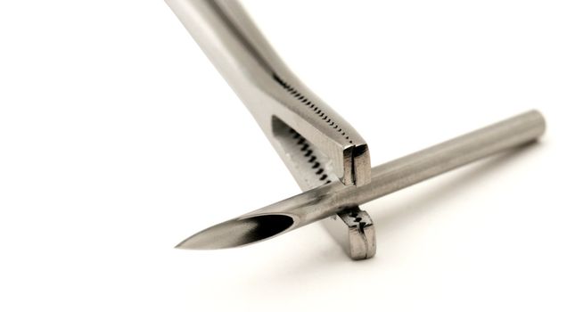 A piercing needle is held in a pair of slotted forceps