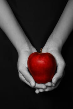 hands holding a red apple in black background
