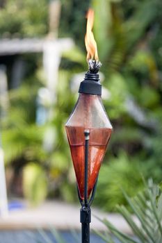 A shot of a red burning tiki torch in a tropical setting
