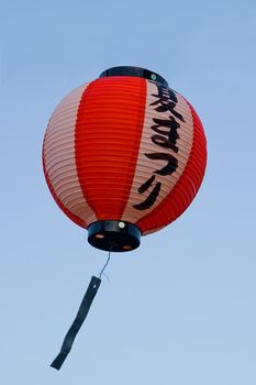 A red and white Japanese lamp floats against a blue sky
