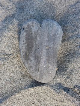 A rock in the shape of a heart sits on a sandy beach
