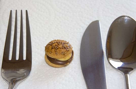 A shot of a tiny hamburger next to a place setting of silverware
