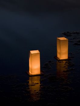 Two floating candlelit lanterns on a lake