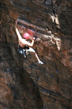 A rock climber works his way up a rock face protected by a rope clipped into bolts. He is wearing a helmet and quickdraws dangle from his harness. The route is in the desert southwest United States. Mt Lemmon, Arizona.