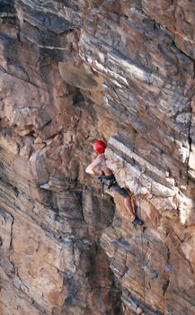 A rock climber works his way up a rock face protected by a rope clipped into bolts. He is wearing a helmet and quickdraws dangle from his harness. The route is in the desert southwest United States. Mt Lemmon, Arizona.