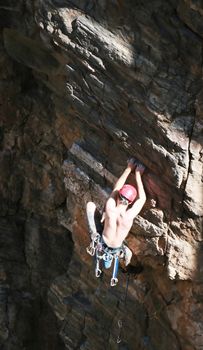 A rock climber works his way up a rock face protected by a rope clipped into bolts. He is wearing a helmet and quickdraws dangle from his harness. The route is in the desert southwest United States. Mt Lemmon, Arizona.