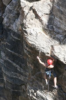 A rock climber works his way up a rock face protected by a rope clipped into bolts. He is wearing a helmet and quickdraws dangle from his harness. The route is in the desert southwest United States. Mt Lemmon, Arizona.